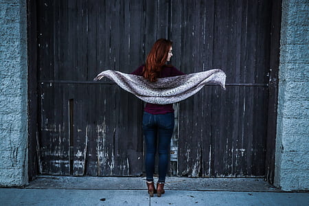 Woman Holding Gray Shawl While Spreading Her Arms Infront of Brown Wooden Door thumbnail