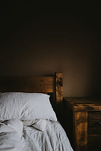 brown wooden nightstand beside bed with white sheet thumbnail