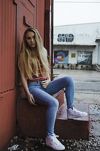 woman in brown and white striped tank top and blue jeans sitting on stairs thumbnail