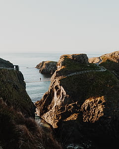 person crossing bridge between mountain near body of water during daytime thumbnail