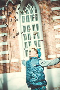 boy wearing blue zip-up vest throwing leaves on air thumbnail