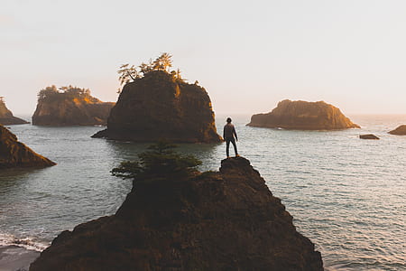 man standing on rock monument in front of body of water thumbnail