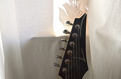 black guitar headstock near white curtain thumbnail