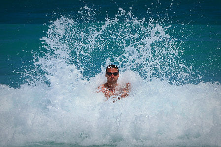 man wearing sunglasses standing between sea waves during daytime thumbnail