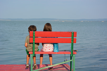 girl and boy sitting on bench near body of water thumbnail