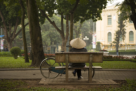 person wearing hat sitting on brown bench near tree thumbnail