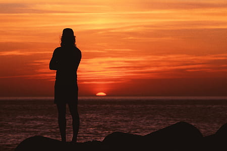 silhouette photography of man standing near body of water during golden hour thumbnail