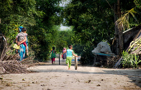 two children running with tires on road near woman standing while carrying child beside trees thumbnail