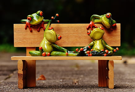 four green ceramic tree frog figurines placed on beige wooden bench miniature close-up photo thumbnail