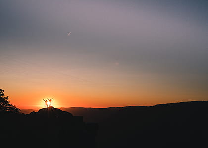 silhouette of two person standing on rock formation with golden hours sun background thumbnail