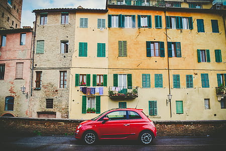 red 3-door hatchback in front of brown concrete building thumbnail