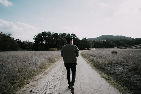 man walking between grass field during daytime thumbnail