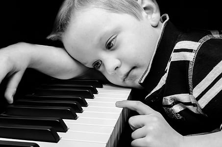grayscale photograph of boy laying on piano keyboard thumbnail