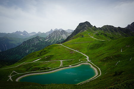 green mountain range with blue body of water under cloudy skies thumbnail