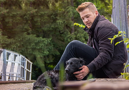 man sitting near black dog thumbnail