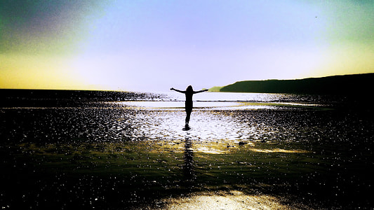 silhouette photography of a person standing with arms wide open surrounded by body of water during golden hour thumbnail