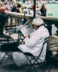 man sitting on black chair while reading newspaper thumbnail
