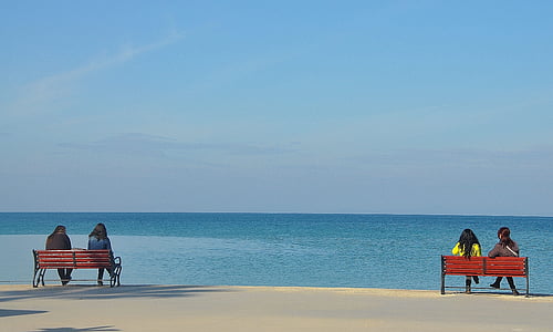 four women sitting on brown wooden bench looking at sea during daytime thumbnail