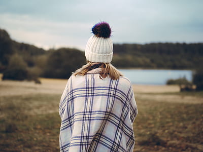 woman wearing white beanie standing on grass field near body of water during daytime thumbnail