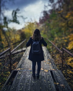 Selective Focus Photography of Woman Wearing Black Overcoat Standing on Wooden Bridge thumbnail