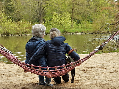 two women wearing black jacket sitting on hammock near body of water during daytime thumbnail