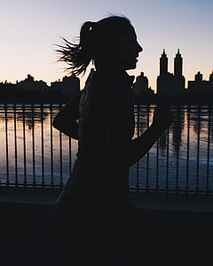 silhouette photo of woman running beside body of water thumbnail