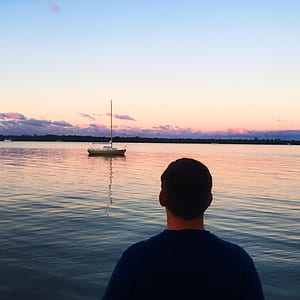 Man in Blue Shirt Near Blue Sea and White Boat Under Blue Sky thumbnail