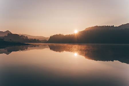 reflection of silhouette of mountain on body of water during golden hour thumbnail