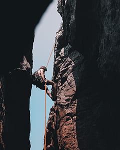 man repelling on gray rocking mountain during daytime thumbnail