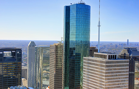blue glass high-rise building surrounded with white buildings under clear blue sky thumbnail