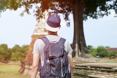 man wearing gray backpack standing near tree at daytime thumbnail