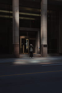 low light photography person in black full-zip jacket standing near commercial building thumbnail