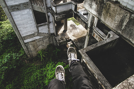 human wearing black pants and pair of gray Vans Old Skool sitting on cliff of abandoned concrete house thumbnail