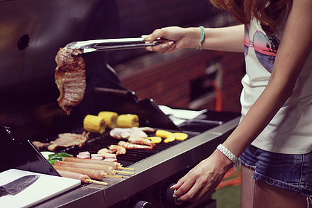woman in white top with blue short shorts holding tongs with grilled steak thumbnail