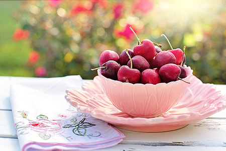 pink bowl of red cherry fruits beside pink floral cloth thumbnail