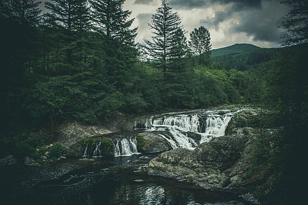 waterfalls surround by trees under cloudy sky thumbnail
