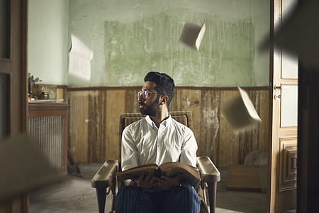 man sitting on brown armchair holding opened book looking sideways thumbnail