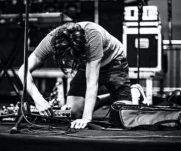 grayscale photo of man setting audio effects devices on floor beside microphone stand and rectangular bag thumbnail