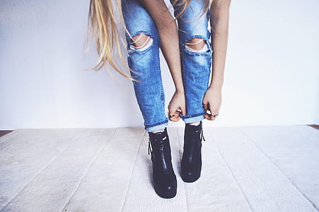 woman wearing blue distressed jeans and pair of black leather boots thumbnail