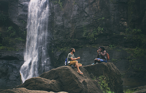 people sitting on rock near waterfalls thumbnail