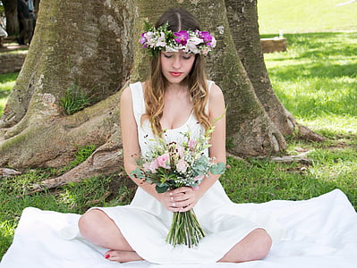 woman seating on white textile holding pink rose flower bouquet against tree thumbnail