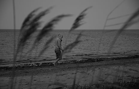 greyscale photo of person in hoodie walking in seashore thumbnail