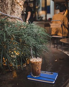 brown liquid with ice in glass on blue book thumbnail