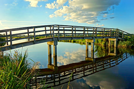 white clouds and clear blue sky reflection on river under gray and brown bridge thumbnail