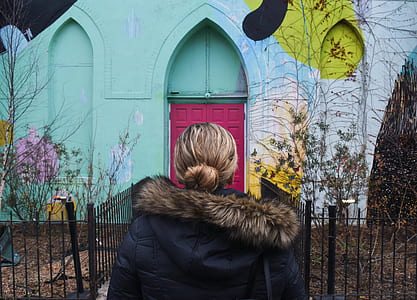 woman wearing black and brown fur hooded jacket looking to pink and teal painted house thumbnail