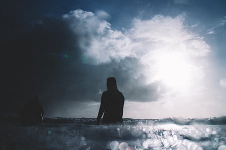 silhouette of person on water under grey and white cloudy sky thumbnail