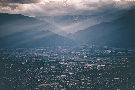 aerial photo of houses near silhouette of mountain under gray clouds with sun rays thumbnail
