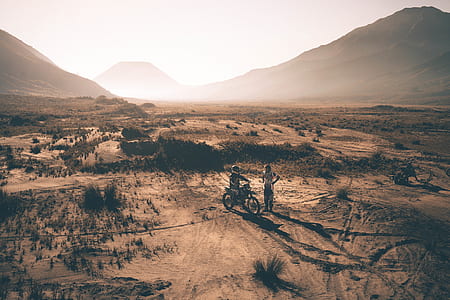 two people on desert with dirt bike photo taken during golden hour thumbnail