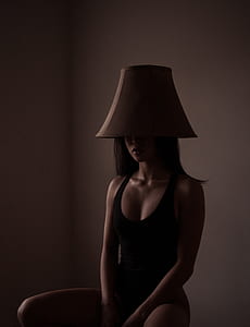 woman wearing black scoop-neck tank top with brown lampshade on her head thumbnail