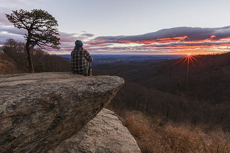 man sitting on the edge of the cliff watching golden hour thumbnail